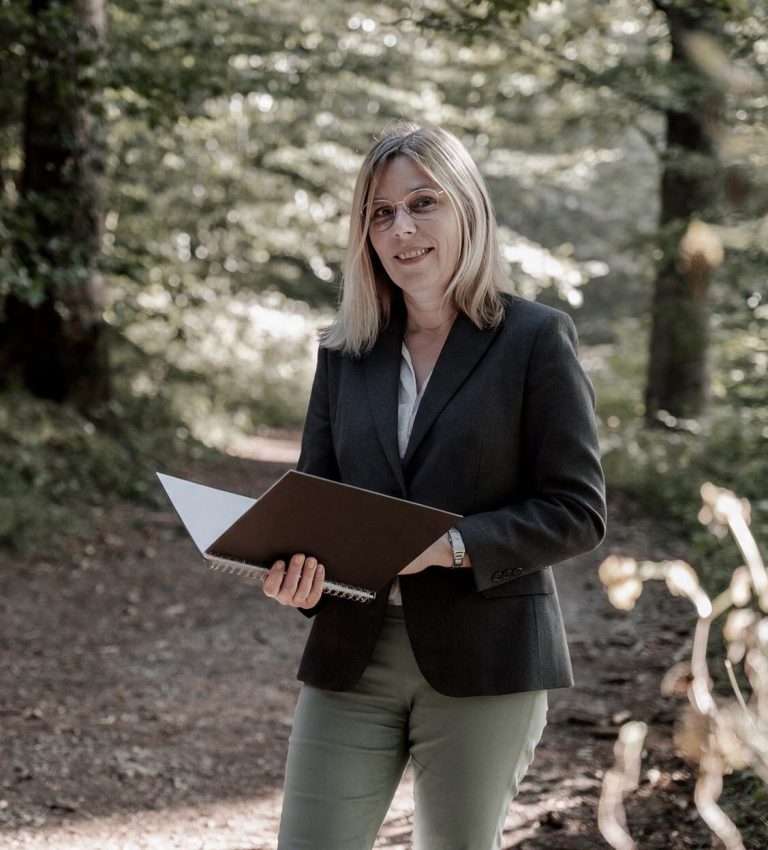 Ines Dorner, Trauerredner, freie Rednerin, Augsburg, Unterallgäu, Landsberg am Lech Frau mit blonden Haaren trägt einen Blazer und liest aus einer Textmappe vor.